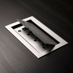 an open metal box on top of a wooden table next to a cell phone charger