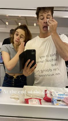 a man and woman standing in front of a counter looking at an electronic device with their mouths open