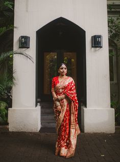 a woman in a red and gold sari standing outside the entrance to a building