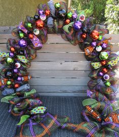 a wreath made out of mesh and decorated with colorful ornaments sits on the back of a wooden bench