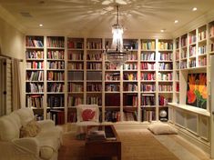 a living room filled with lots of books on top of a book shelf next to a white couch