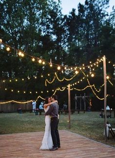 a bride and groom sharing their first dance on the deck with string lights strung above them