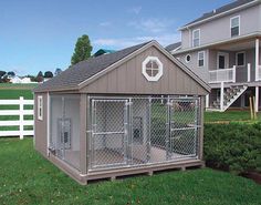 a dog kennel in the middle of a yard with a fence and two houses behind it