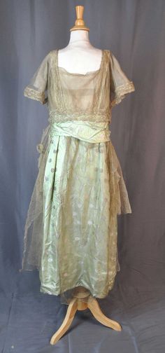 "PATTERNED SILK SATIN FLAPPER EVENING DRESS GOLD METALLIC LACE TRIM AND NETTING 1920s 1920's era Flapper evening dress. One piece in construction, double short sleeves, gold metallic lace netting streamer panels drapes its sides. Skirt in light green brocade satin patterned with striped circles. Bodice with a fine gold metallic netting and gold metallic floral trim, with scoop neck and scoop back. The metallic lace drapes over the shoulders and ends at sash waist line. Many hook and eye and snap 1920s Evening Gowns, Satin Evening Dress, Dress One Piece, Silk Evening Dress, Gold Evening Dresses, Satin Evening Dresses, 1920s Dress, Clothing And Textile, Antique Clothing