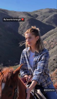 a woman riding on the back of a brown horse next to a mountain range with hills in the background