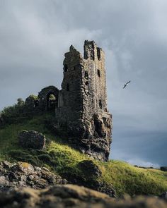 an old stone castle sitting on top of a lush green hillside under a cloudy sky