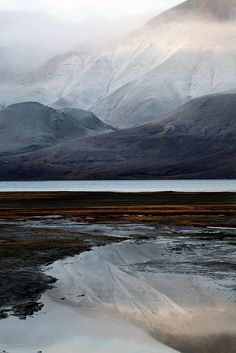 the mountains are covered in snow and reflecting on the water's surface with low lying clouds