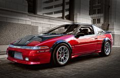 a red sports car parked in front of a tall building on a brick road with its hood up