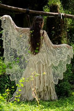 a woman with long hair wearing a white crochet shawl in the woods