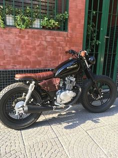 a black motorcycle parked in front of a brick building with green doors and window frames