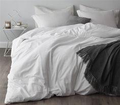 an unmade bed with white linens and grey throw pillows on the bottom half