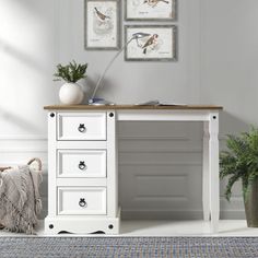 a white desk with three pictures on the wall and a potted plant next to it