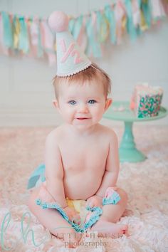 a baby is sitting on the floor wearing a birthday hat and blue diaper with pink frosting