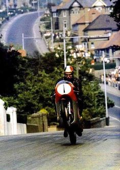 a man riding a motorcycle down a street with houses in the background on either side