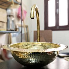 a gold colored bowl sitting on top of a wooden table next to a metal faucet