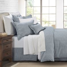 a bed with blue and white linens in front of a brick wall next to a window