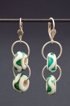 two earrings with green and white swirls hanging from hooks on a metal rod against a black background