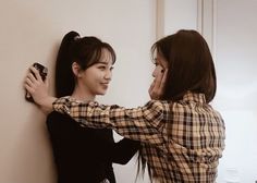 two young women standing next to each other near a wall and one is holding a cell phone