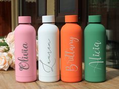 three different colored water bottles sitting on top of a wooden table next to white flowers