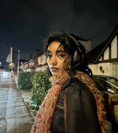 a woman wearing headphones standing on the side of a road at night with buildings in the background