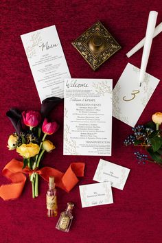 the wedding stationery is laid out on top of the red table cloth with flowers