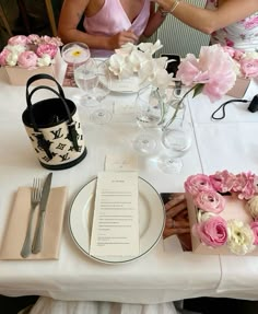 two women sitting at a table with plates and flowers in vases on the table