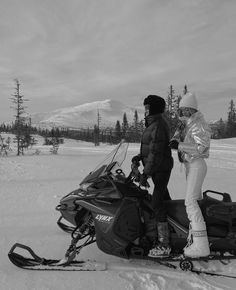 two people standing next to a snowmobile in the snow