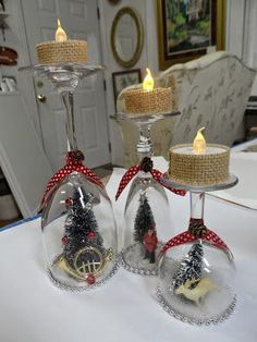 three wine glasses sitting on top of a table with christmas decorations in them and lit candles