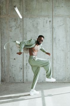 a man in green pants and white sneakers is dancing with his arms stretched out to the side