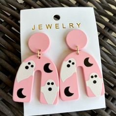 two pink and white earrings with black dots on the bottom, one is shaped like a dog