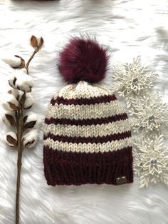 a knitted hat with a pom - pom sits next to cotton flowers