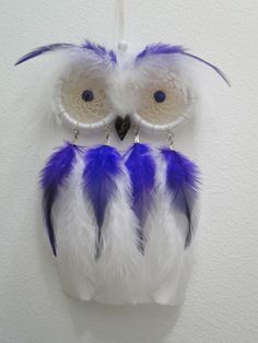 an owl ornament hanging on the wall with blue and white feathers attached to it