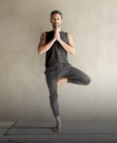 a man standing on one leg with his hands in the air while wearing a black shirt and grey pants