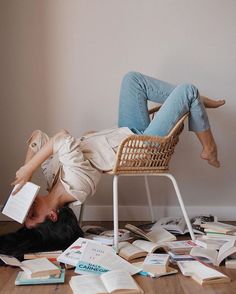 a woman laying on the floor with her head down reading a book while surrounded by books