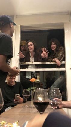 a group of people sitting around a table with wine glasses on top of it and one person holding up his hand