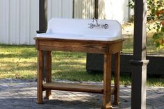 an old fashioned sink sitting on top of a wooden stand in front of a house