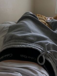 an unmade bed with a person laying on it's side wearing a hoodie