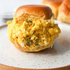 an egg salad sandwich on a plate with croissants in the background