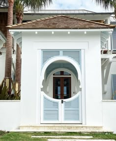 a large white house with palm trees in the front yard and an arched doorway leading into it