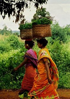 two women walking down a dirt road carrying baskets on their heads