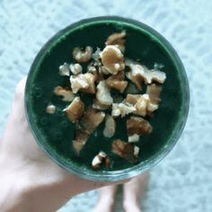 a person holding up a green smoothie with walnuts and other things in it