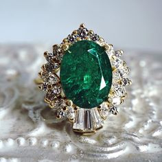 an emerald and diamond ring sitting on top of a table