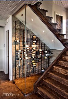 a glass case with wine bottles in it on the side of a stair case next to a set of stairs