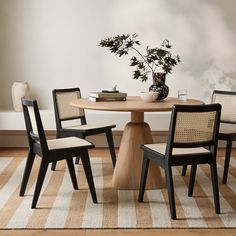 a round table with four chairs and a vase on top is in front of a striped rug