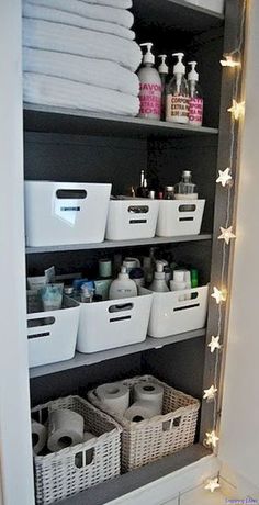 an organized bathroom closet with white baskets and lights