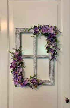 an old window is decorated with purple flowers and greenery on the front door,