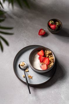 a bowl of granola with strawberries and yogurt on a plate next to a spoon