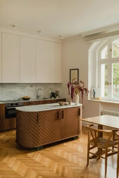 a kitchen with wooden flooring and white cupboards next to a dining room table