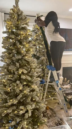 a woman standing on a ladder next to a christmas tree