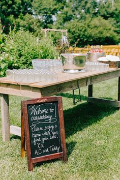 a wooden table with a chalkboard sign sitting on top of it in the grass